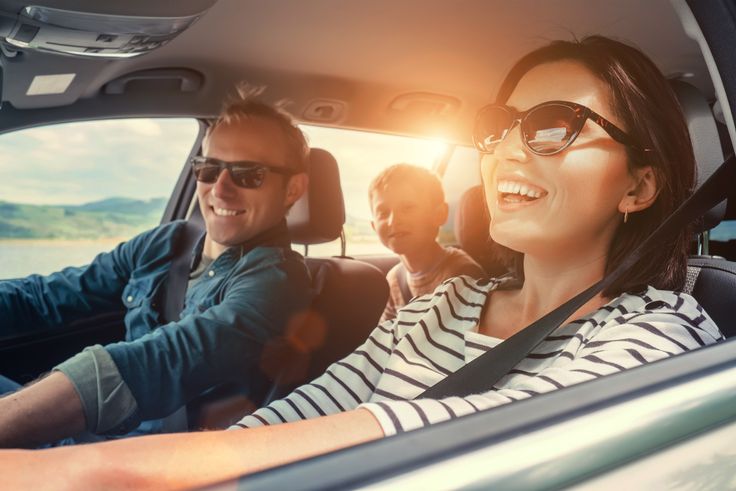 Famille souriante en voiture, conduite sous un soleil couchant.