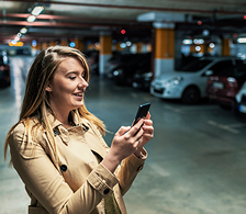 Personne utilisant un smartphone dans un parking souterrain avec des voitures stationnées en arrière-plan.