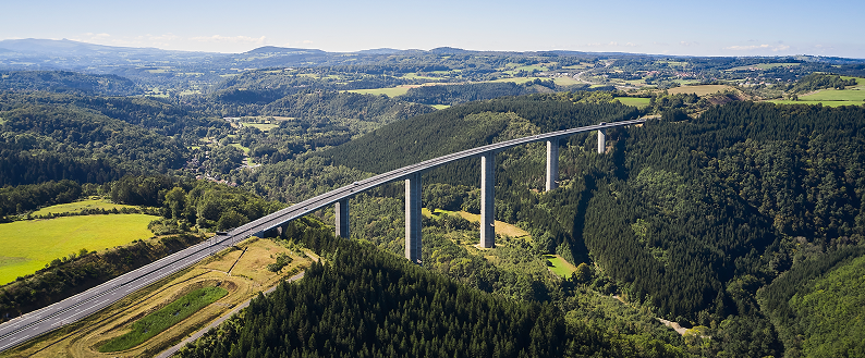 Viaduc autoroutier traversant une vallée boisée, vu en hauteur au‑dessus de paysages verdoyants.